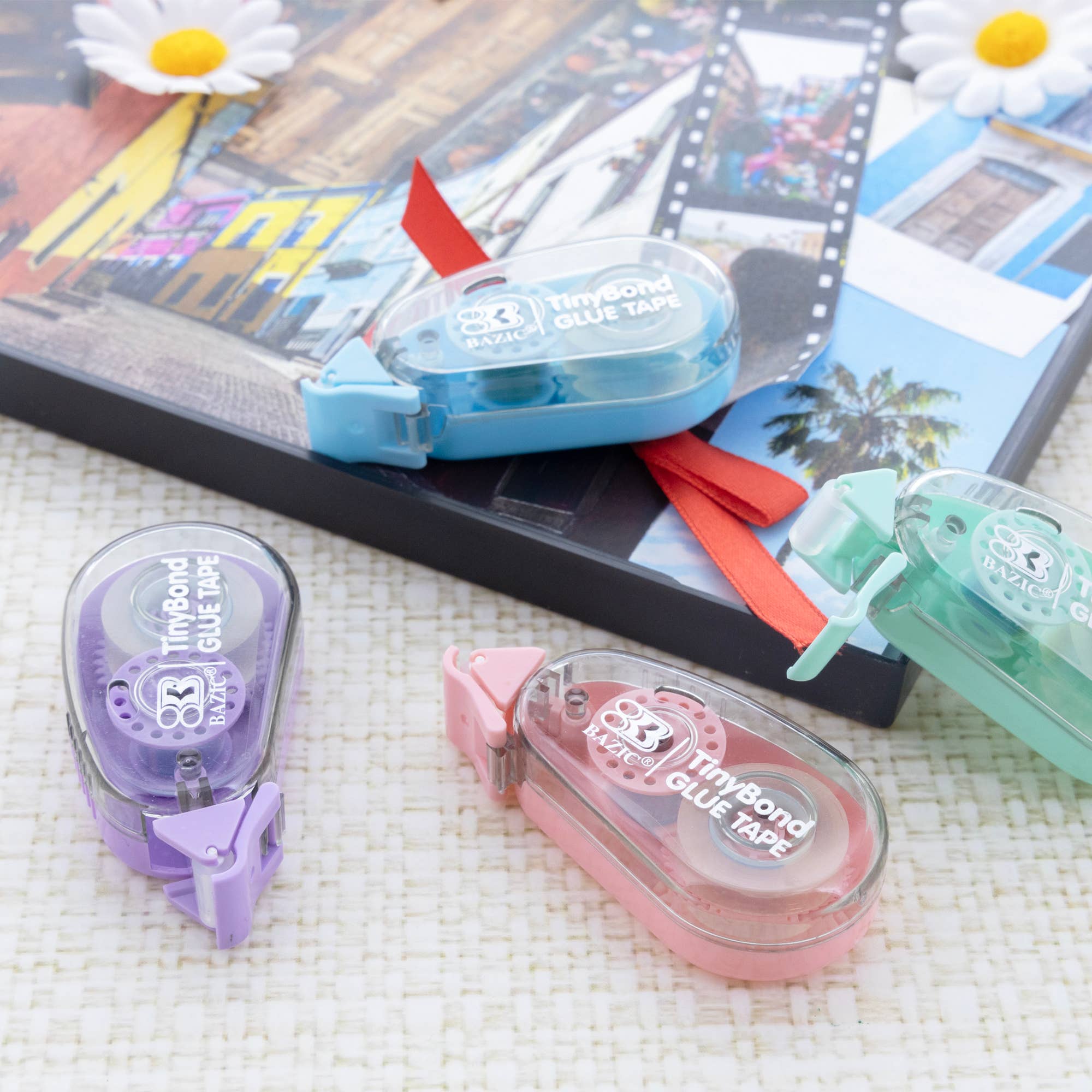 Three small containers of Tinybond glue tape on a textured surface with a colorful background.